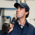 Male worker in blue uniform confidently using a power drill in an industrial setting for A-Plus Air Conditioning services.