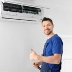 Smiling technician in blue shirt thumbs-up by air conditioning unit, showcasing A-Plus Air Conditioning services.