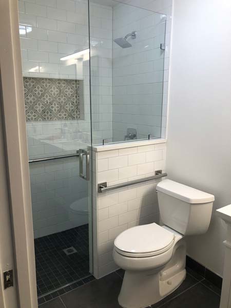Modern bathroom featuring a walk-in shower with glass enclosure, grab bars for accessibility, and a white toilet, highlighting ADA-compliant aging-in-place renovation by A-Plus Air Conditioning & Home Solutions.