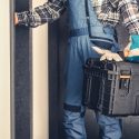 Person in plaid shirt and blue overalls carrying a toolbox in doorway, representing practical HVAC and home repair services.
