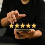 Person&rsquo;s hands using a smartphone showing five golden stars for HVAC ratings by A-Plus Air Conditioning & Home Solutions.