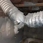 Metal ductwork in utility space with silver material, connection joint, and visible wear, indicating needed maintenance.