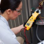 Woman wearing safety goggles and gloves using a multimeter for air conditioning maintenance at A-Plus Home Solutions.