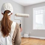 Painter with a paint roller on a gray wall, illustrating home improvement by A-Plus Air Conditioning & Home Solutions.