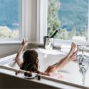 A person relaxing in a bathtub with a mountains view, champagne bottle nearby, highlighting luxury and home comfort.