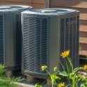 Metallic air conditioning units with green foliage and yellow flowers, representing A-Plus HVAC solutions outdoors.