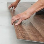 Hands installing laminate flooring for energy-efficient renovations by A-Plus Home Solutions.