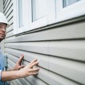 Construction worker inspecting siding and window frame, highlighting safety in air conditioning home improvement projects.