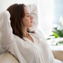 Woman relaxing on a sofa with indoor plants, showcasing tranquility in a comfortable home setting by A-Plus Air Conditioning.
