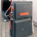 Goodman furnace in a utility area, showcasing gray and red accents, connected to heating system. A-Plus home services.