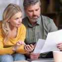 Couple reviewing home remodeling documents and a phone for A-Plus Air Conditioning in a casual indoor setting.
